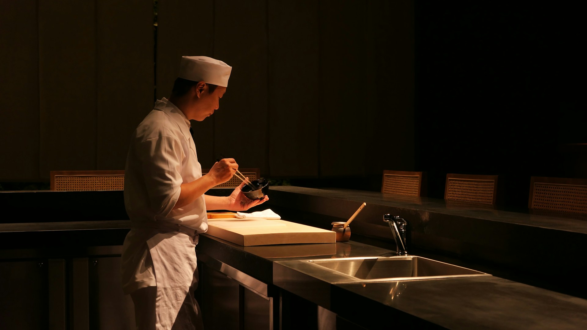 A chef at the Loud Fish counter, plating a bowl under a low warm light